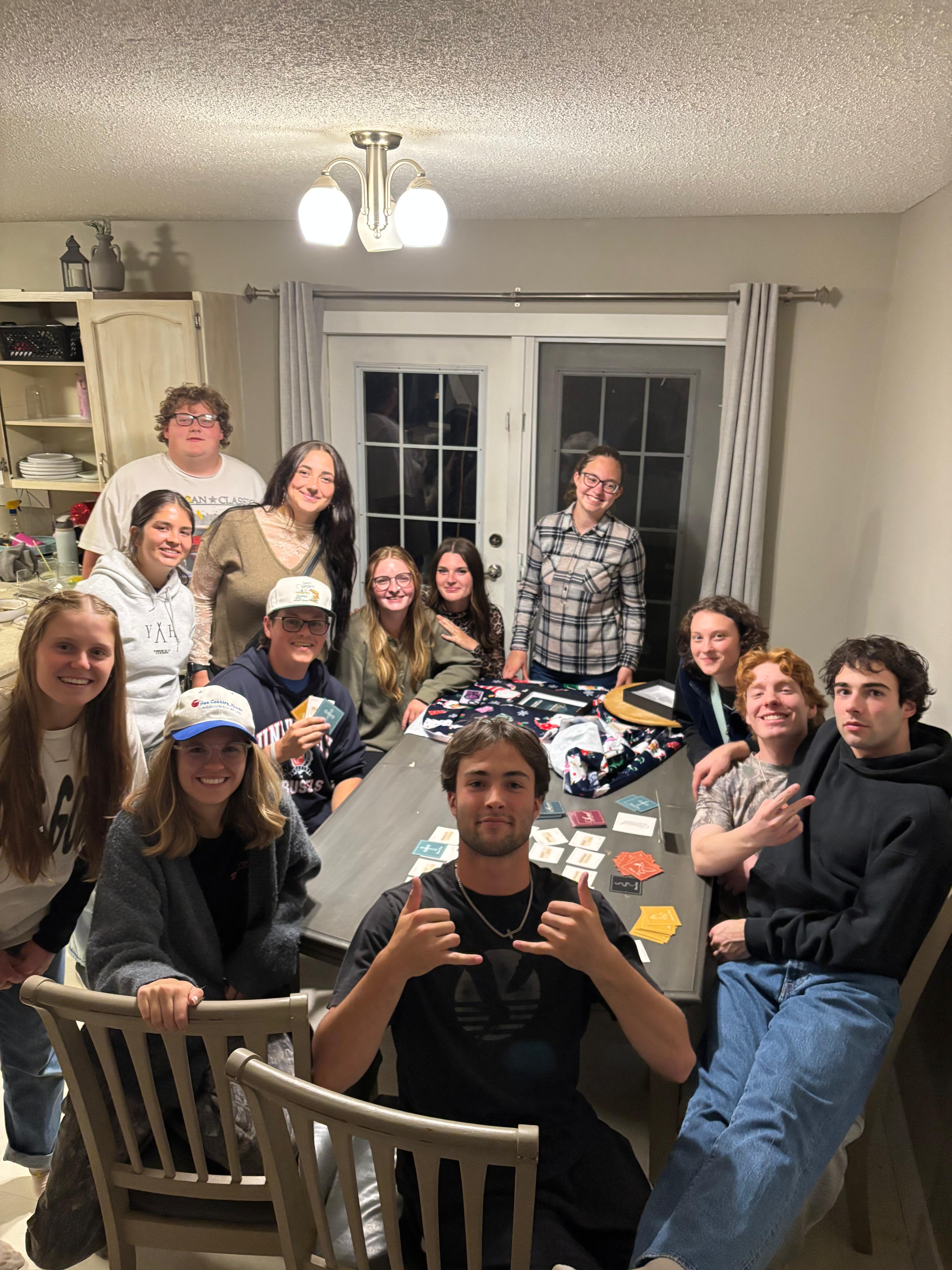 Large group of friends gathered around a home dining table playing Revival
